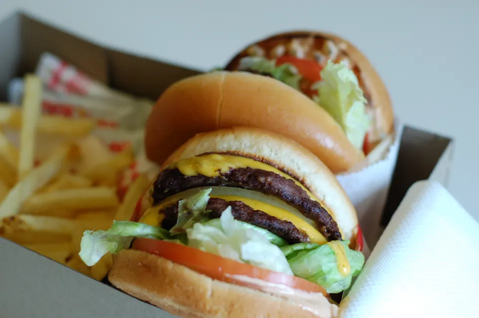 An In-N-Out Double-Double cheeseburger in narrow depth-of-field focus with a second burger and fries blurred in the back en los-angeles