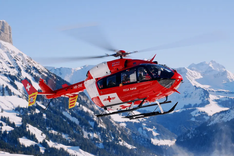 Helicóptero de rescate alpino de emergencia en vuelo frente a cumbres nevadas de alta montaña.