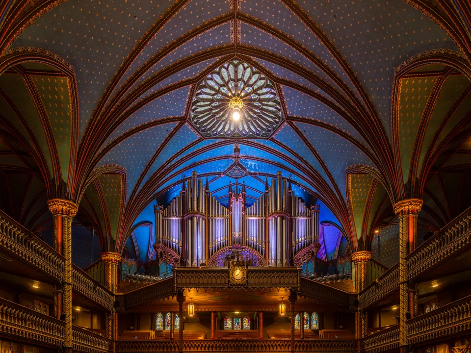 Nave principal neogótica iluminada en tonos azules y dorados en la Basílica de Notre-Dame de Montreal.