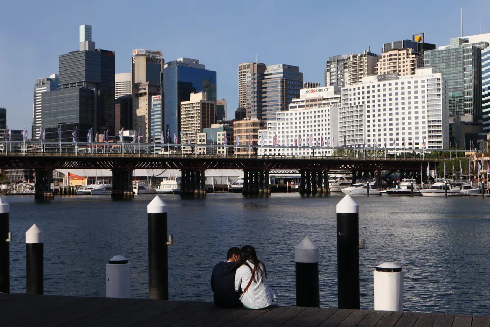 Paseo marítimo y terrazas gastronómicas a orillas del agua en Darling Harbour al atardecer.