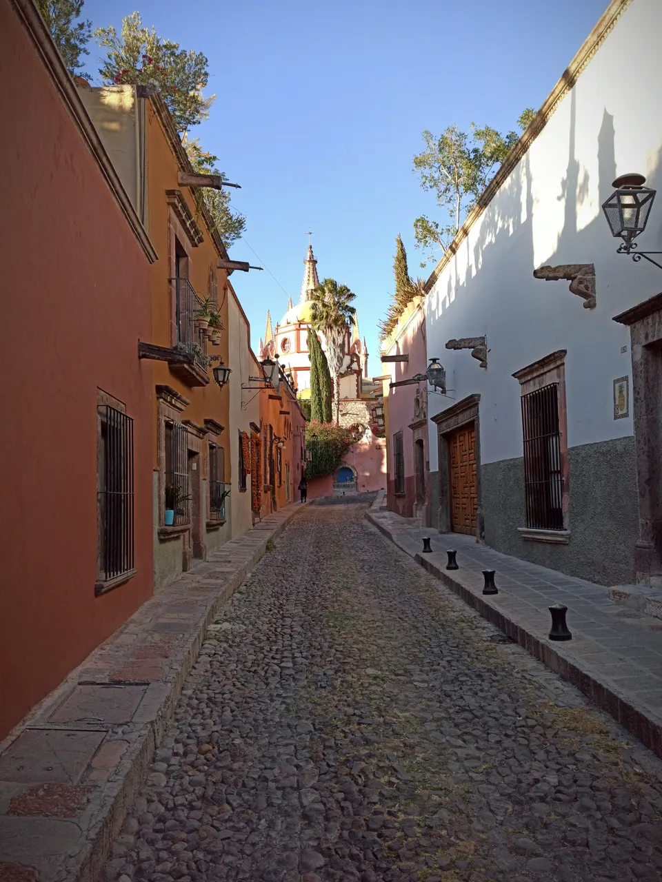 Perspectiva clásica de la Calle Aldama con adoquines coloniales, buganvilias y la Parroquia al fondo.