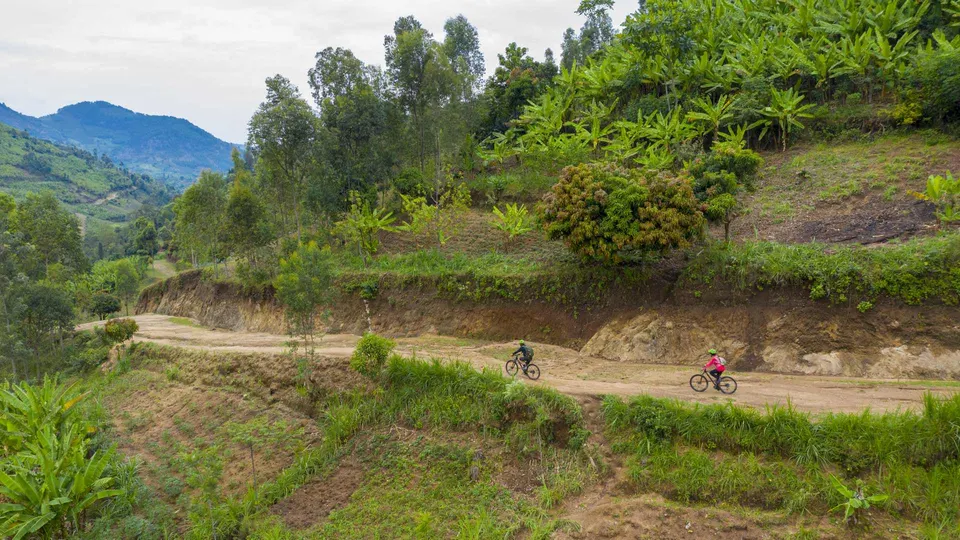 Ciclistas recorriendo los caminos de tierra del Congo Nile Trail con vistas panorámicas al lago.