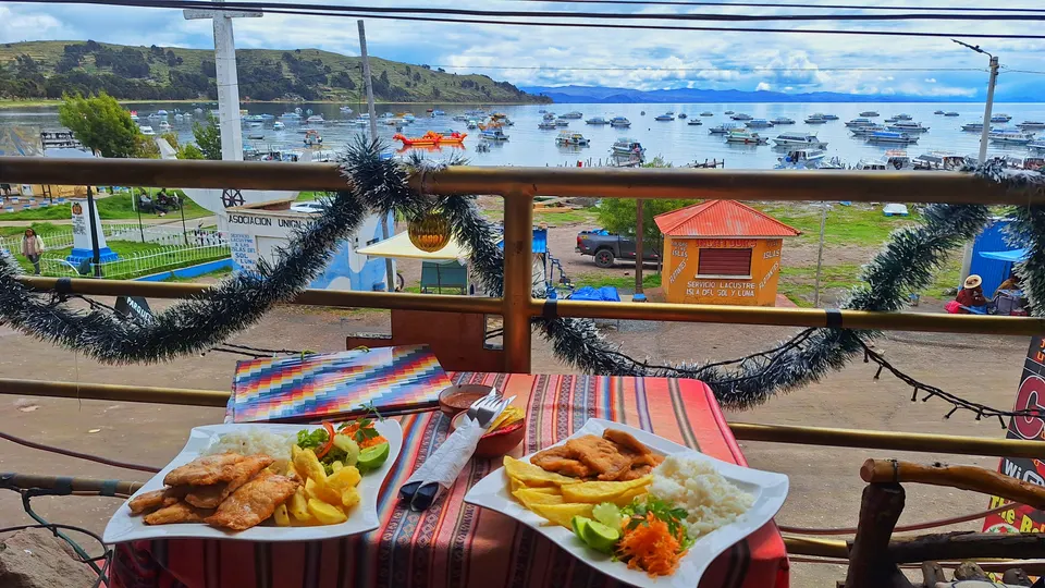 Plato tradicional de trucha frita fresca servida con guarniciones frente a la bahía de Copacabana.