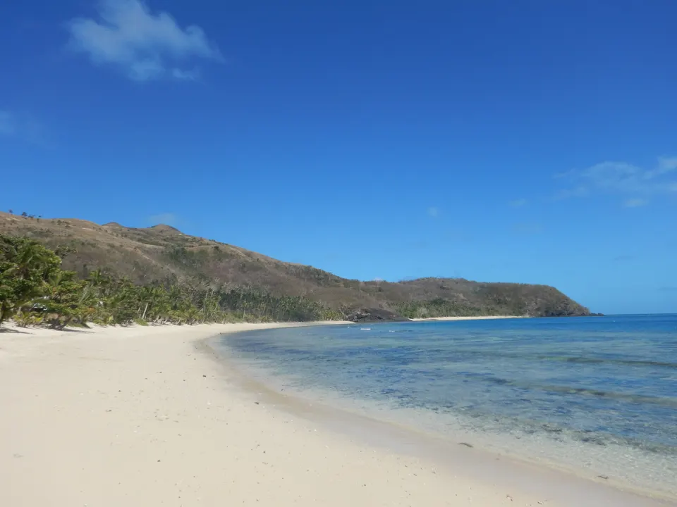 Bahía costera resguardada con arena blanca y colinas boscosas en la isla de Naviti en las Yasawa.