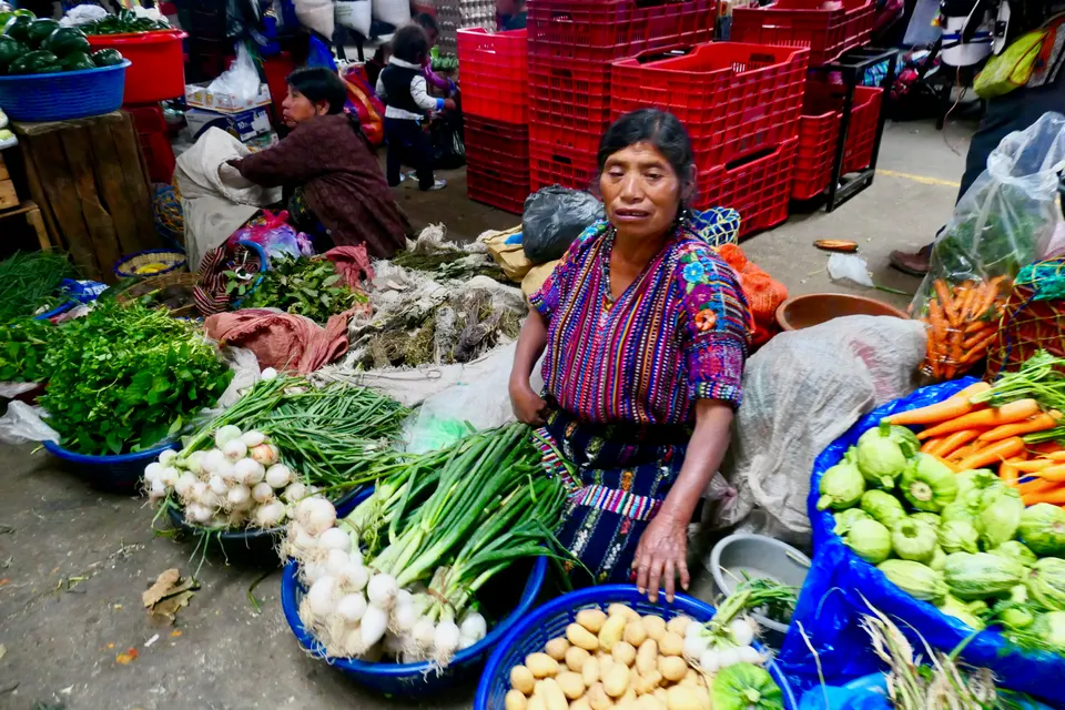 Puestos de hortalizas frescas y comerciantes luciendo trajes mayas tradicionales en el mercado de Sololá.