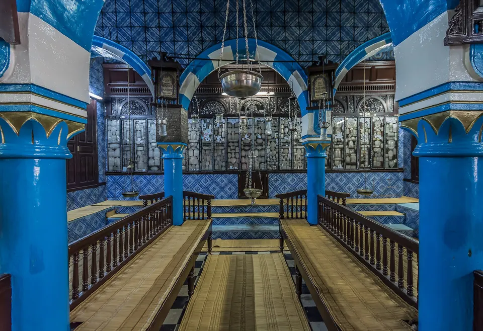 Interior sagrado de la milenaria Sinagoga de la Ghriba con arcos turquesas y azulejería.