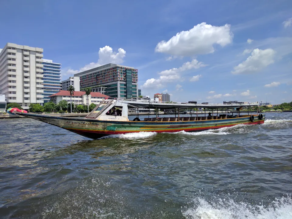 Embarcaciones tradicionales navegando por el río Chao Phraya con templos de fondo en Bangkok.