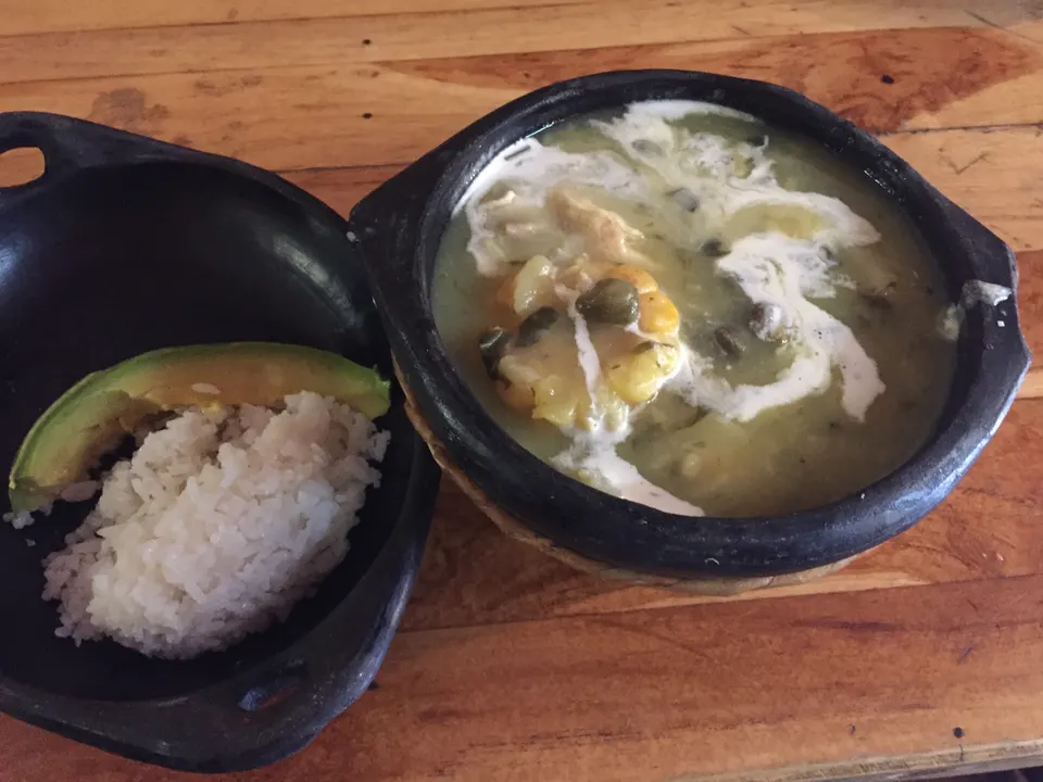 Sopera de barro con humeante ajiaco santafereño con pollo desmechado, maíz tierno, alcaparras, crema y aguacate