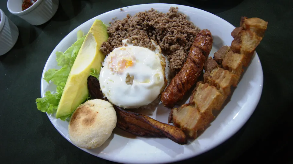 Generosa bandeja paisa con chicharrón crujiente, frijoles cargamanto, plátano dulce, huevo y arepa