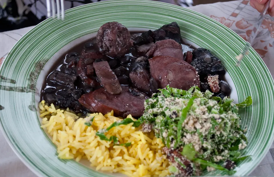 Tradicional feijoada carioca completa servida en cazuela de barro con arroz blanco, farofa, couve mineira y gajos de naranja fresca.
