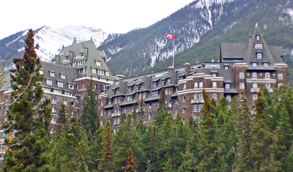 El majestuoso hotel castillo Fairmont Banff Springs emergiendo entre los bosques de pinos junto a Bow Falls.