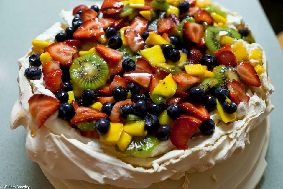 Deliciosa pavlova australiana decorada con crema batida, maracuyá y frutas rojas frescas.