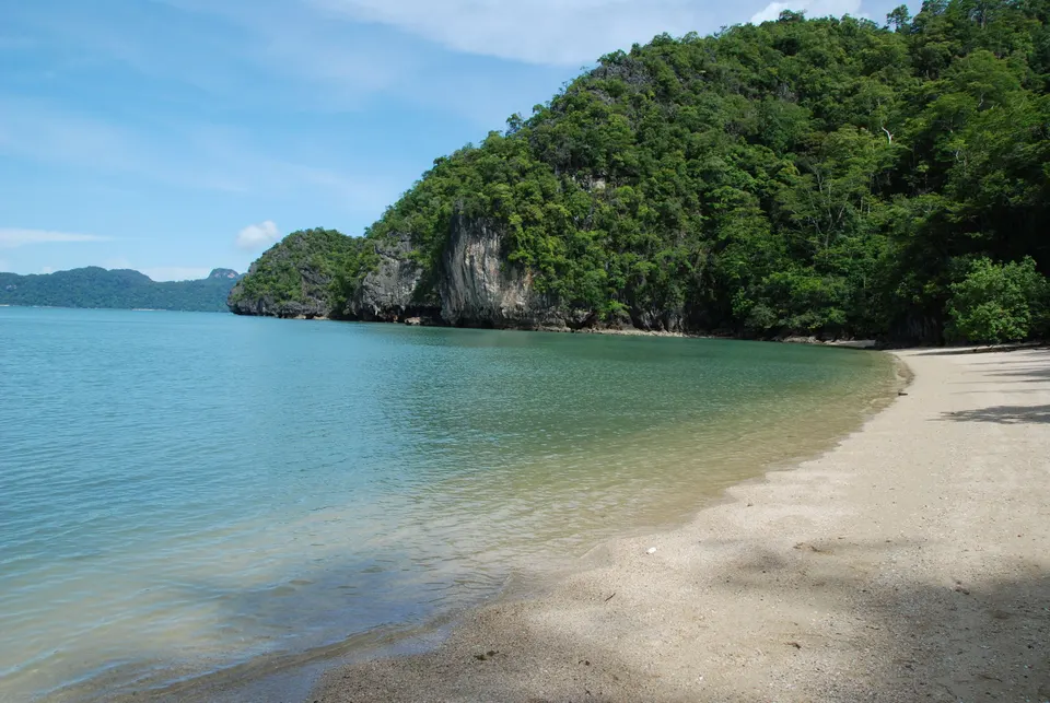 Bancos de arena fina y aguas turquesas en calma frente a islotes de piedra caliza en Tanjung Rhu.