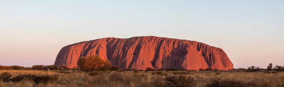 El monolito sagrado de Uluru brillando en tonos rojizos durante la puesta de sol en el desierto australiano.