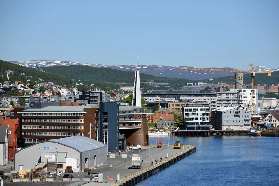 Muelles con barcos pesqueros y almacenes de madera reflejados en el agua al anochecer en Tromsø.
