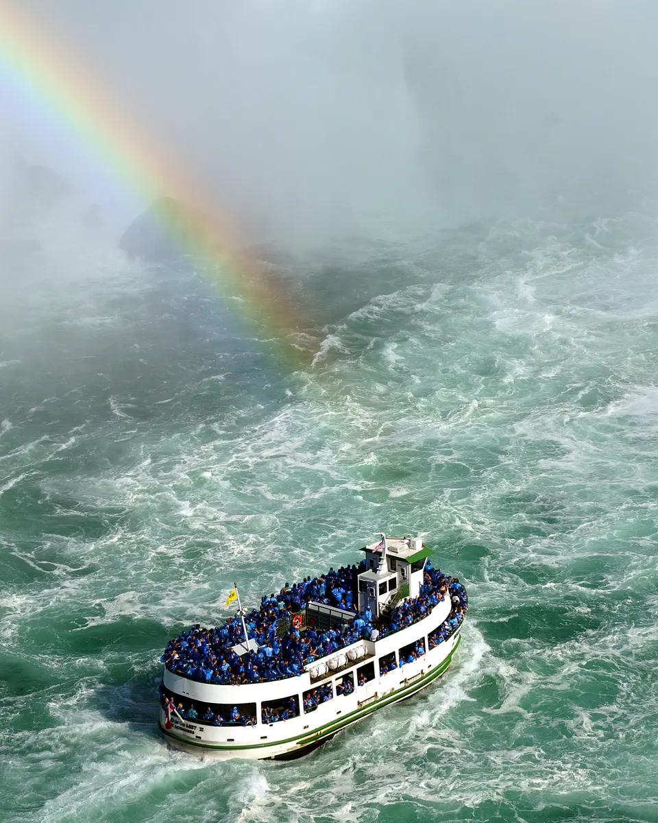 Paseo en barco con turistas protegidos con impermeables contemplando cataratas.