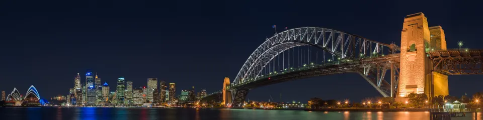 Vista panorámica de la bahía de Sídney con la Opera House, el Harbour Bridge y el horizonte al atardecer.