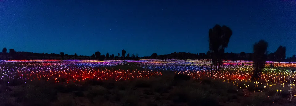 Miles de esferas de luz iluminando el desierto nocturno frente a Uluru en la obra Field of Light.