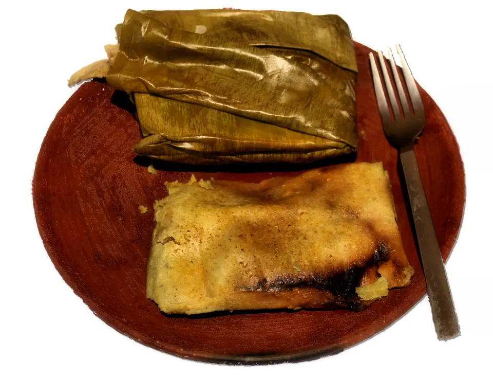 Photo of wrapped and unwrapped Tamales Oaxaqueños. The tamales consists of masa, chicken and mole negro, wrapped in pla en oaxaca