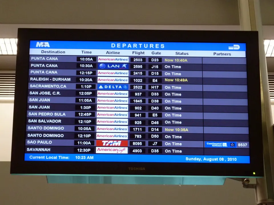 Panel de información de vuelos en aeropuerto con avisos de retrasos y puertas de embarque.