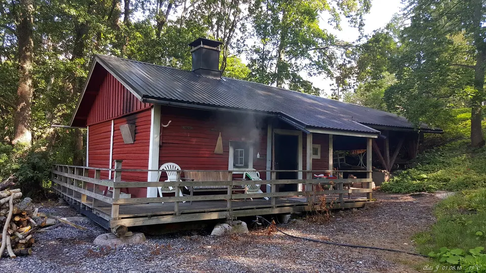 Cabaña de madera de sauna tradicional finlandesa con pasarela de madera sobre un lago en calma.