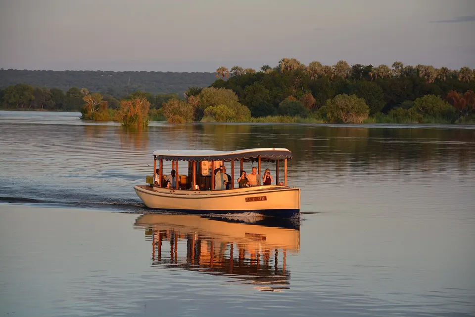 Barco de safari fluvial navegando plácidamente por el río Zambeze durante el crepúsculo.