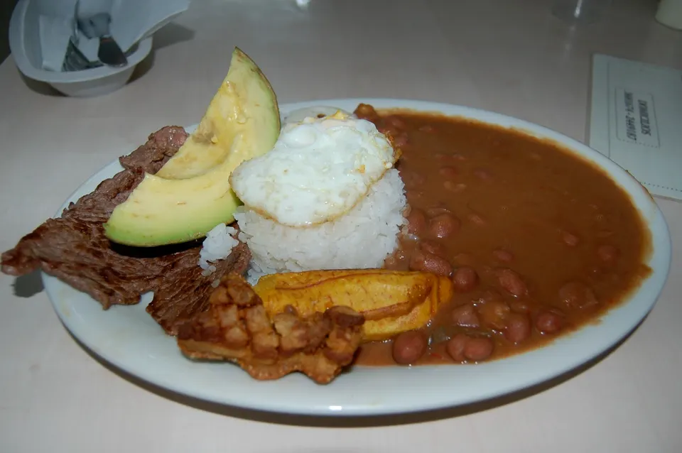 Contundente bandeja paisa colombiana con frijoles, arroz, chicharrón crocante, carne en polvo, huevo frito, aguacate y arepa