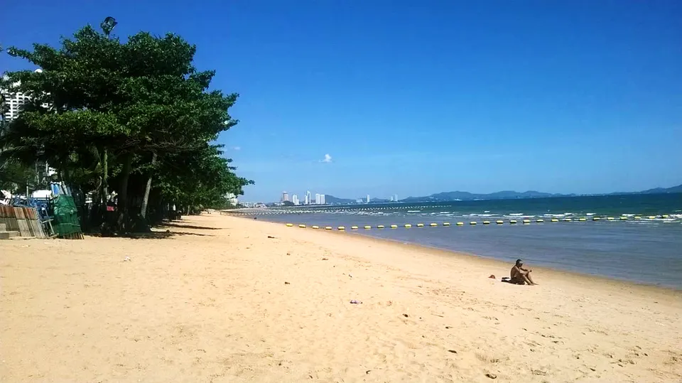 Extenso paseo marítimo bordeado de palmeras y aguas serenas en la playa de Jomtien, Pattaya.