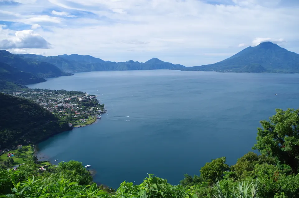 Vista panorámica del Lago de Atitlán con aguas de color azul profundo y los volcanes circundantes en el horizonte.