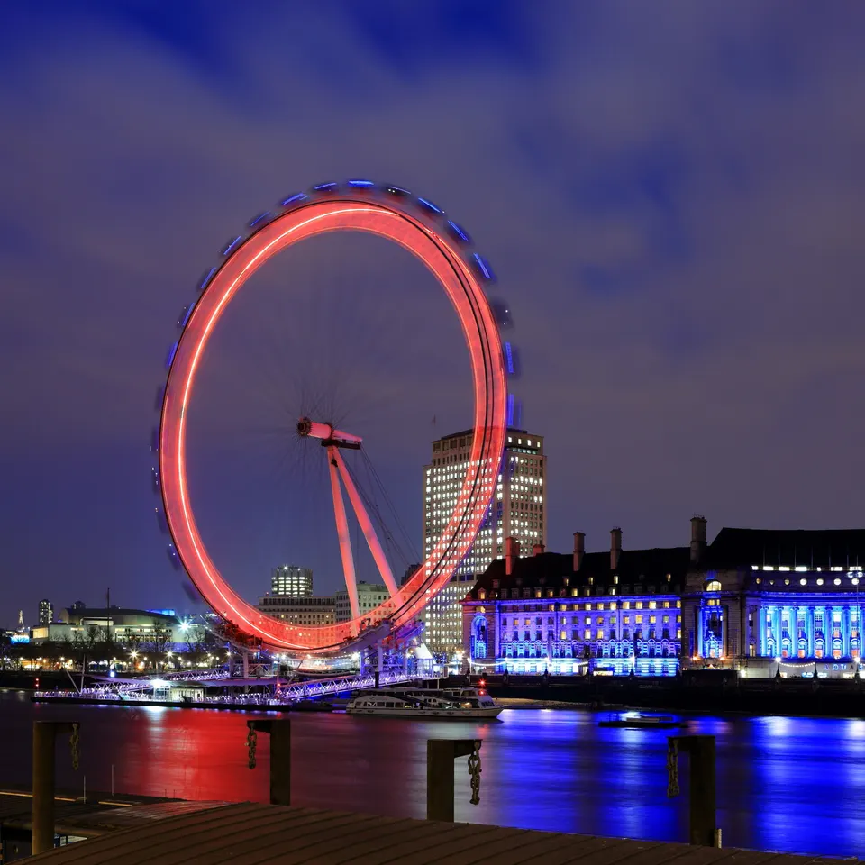 The London Eye iluminado de noche con larga exposición reflejándose en las aguas del Támesis.