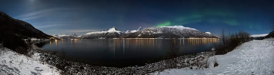Aurora boreal de color verde iluminando el cielo invernal sobre los fiordos de Noruega.