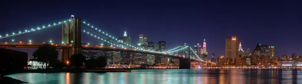 El puente de Brooklyn iluminado de noche, con el perfil de Manhattan detrás.