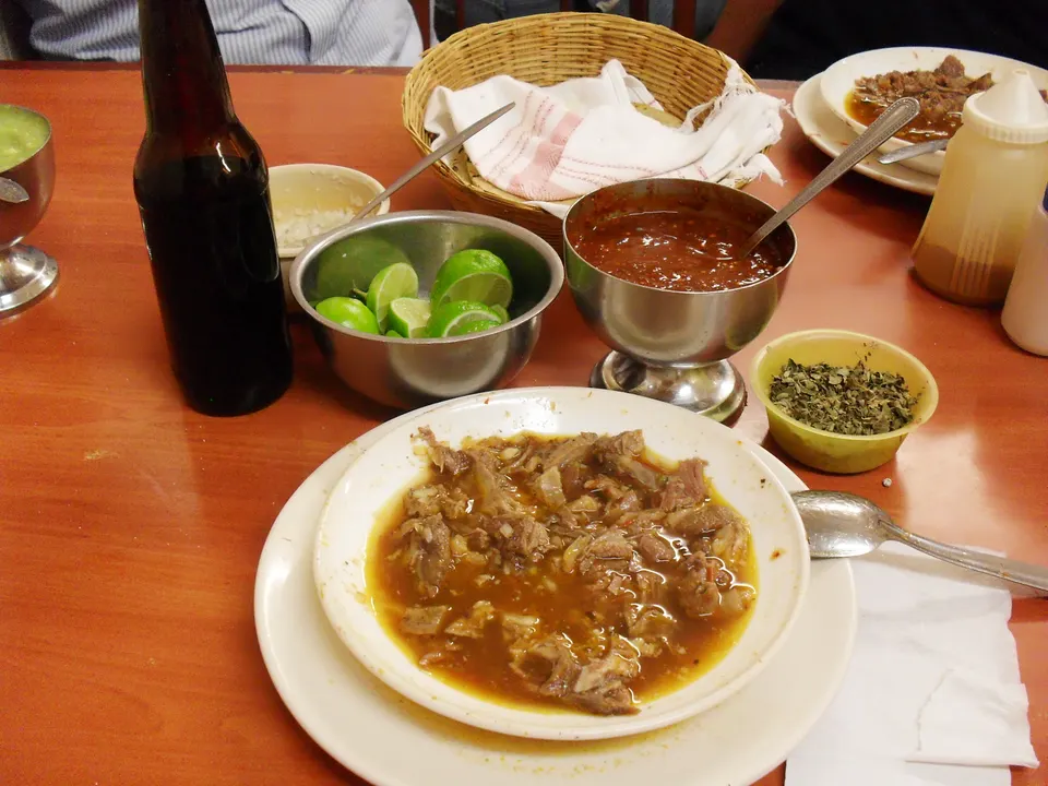 Tradicional birria tatemada jalisciense servida con consomé, limones y tortillas calientes.