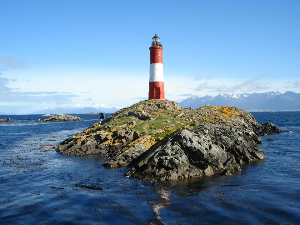 El emblemático Faro Les Eclaireurs pintado a franjas rojas y blancas sobre un islote rocoso del Canal Beagle.