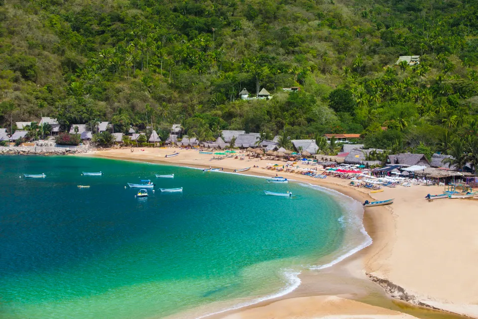 Tranquila ensenada de arena dorada y palapas frente al mar en el pueblo costero de Yelapa.