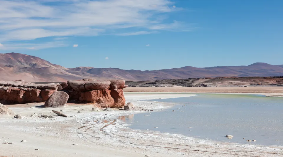 Manto de rocas rojizas volcánicas bordeando las aguas turquesas del Salar de Talar.