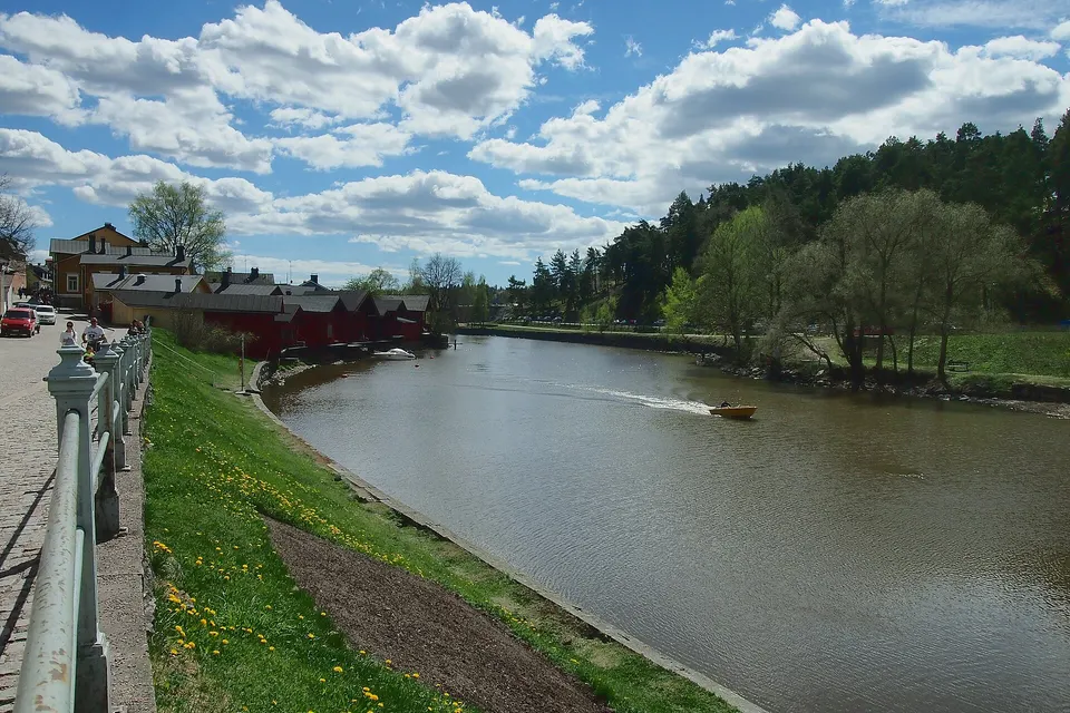 Paseo peatonal ribereño con barcos amarrados y terrazas estivales frente al río Porvoonjoki.
