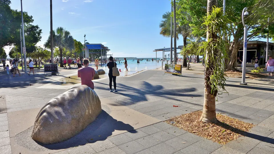 Laguna artificial de agua salada en Cairns Esplanade con palmeras tropicales y montañas de fondo.