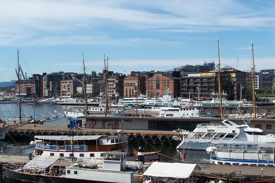 Paseo marítimo de Aker Brygge con terrazas gastronómicas y barcos amarrados en el muelle.