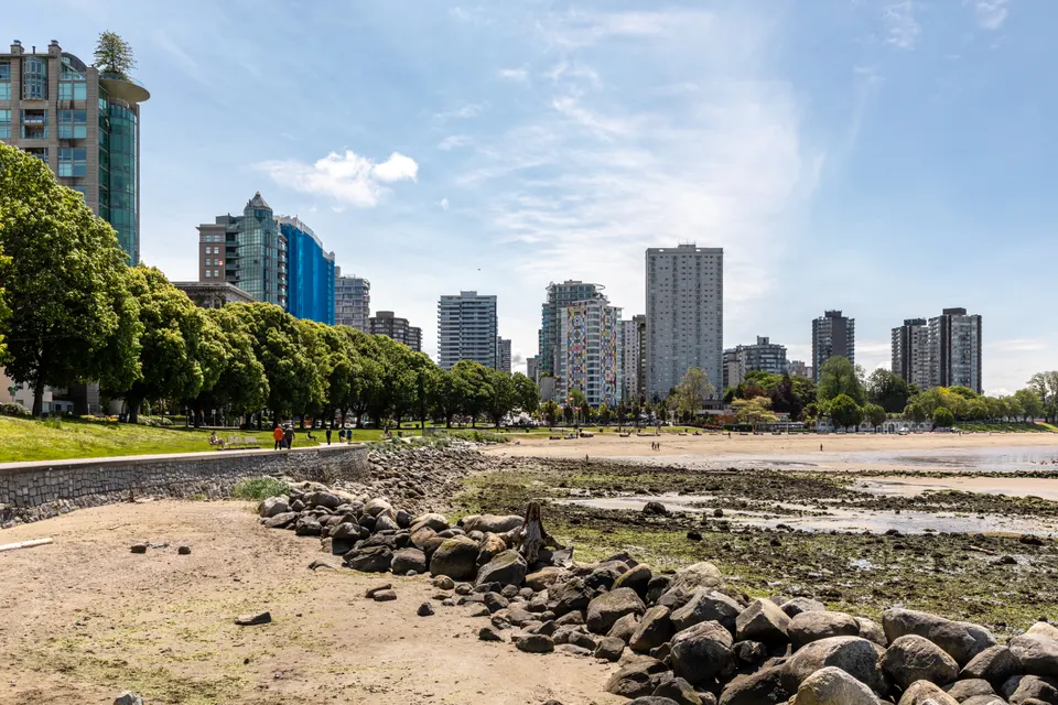 Paseantes y troncos de cedro en la orilla de English Bay Beach con vistas abiertas hacia el estrecho de Georgia.